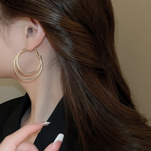 Close-up of golden multi-layered twist hoop earrings worn by a model from a side view