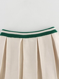 Detail of cream pleated knit skirt showing green striped waistband and fabric texture