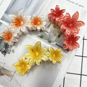 Detailed view of three glossy frangipani flower hair claws in white orange and yellow