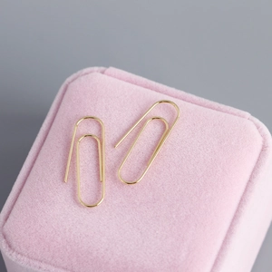Detailed view of gold safety pin earrings on a pink velvet jewelry display box