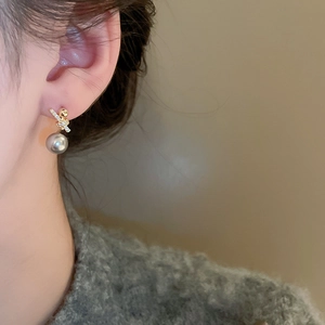 Detail of gold geometric earrings with sparkling zircon and gray pearl on a model
