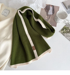 Close-up of dark green knitted scarf with white trim and brown leather logo tag
