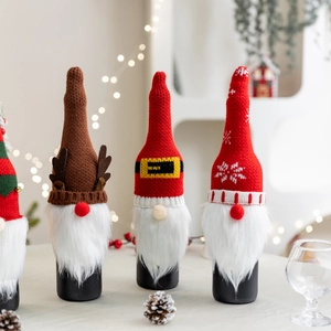 Drei festliche gestrickte Weihnachtsweinflaschenhüllen mit Zwergenmotiven auf dem Tisch