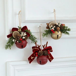 Three assorted Christmas bells with pine cones and red berries on a white wood wall