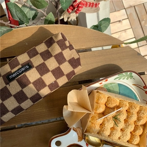 Close-up of checkers knit corduroy pencil case on a wooden desk with a dessert accent