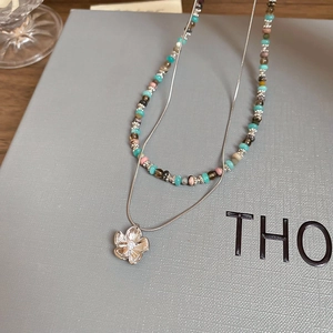 Detail of double-layer beaded necklace with metallic flower pendant and small pearl