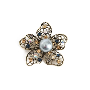 Detailed close-up of retro floral brooch with bronze openwork, pearls and colorful rhinestones