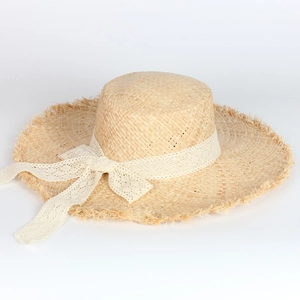 Detail of raffia straw hat with raw fringe edges and cream lace bow tie decoration