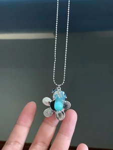 Nahaufnahme eines silbernen Blumenanhängers mit blauem Katzenaugenstein an einer Kugelkette