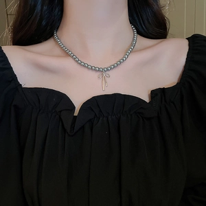Detail view of dark grey beaded choker with a golden bow pendant on model's neck
