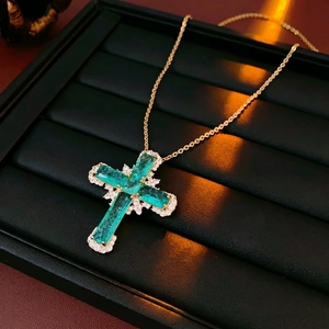 Golden cross necklace with emerald-cut green gems and white zircon on a black display