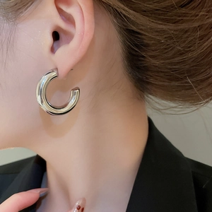 Close-up of polished silver C-shaped chunky hoop earrings worn by a female model