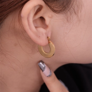Close-up of model wearing thick gold waterdrop C-shape earrings with polished finish