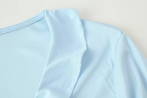 Detail of light blue knit top featuring ruffled V-neckline and elastic fabric texture