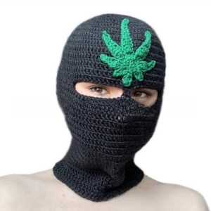 Detail of handmade black knitted balaclava with green leaf embroidery on the forehead