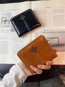 Detail view of square leather coin purses in black and brown with floral metal emblem
