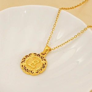 Gold round necklace featuring a vintage镂空 engraved letter E pendant on a ceramic dish