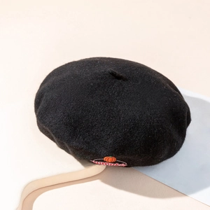Klassische schwarze Wollbaske mit orangefarbener Kürbisbestickung auf beigem Sockel