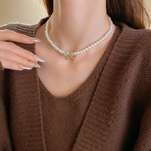 Détail d'un collier de perles élégant avec pendentif nœud en cristal porté par une femme