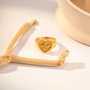 Artistic detail of gold heart signet ring featuring a 3D angel relief on beige background