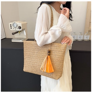 Detail of straw tote bag featuring orange tassels and decorative wooden beads