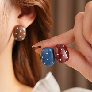 Dettaglio di orecchini ovali a pois in resina nei colori marrone, blu e bordeaux scuro