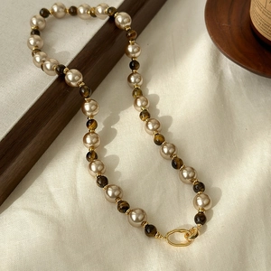 Tiger eye stone and pearl beaded necklace with gold metal clasp on a textured surface
