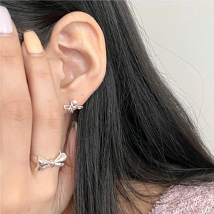 Close-up of polished 925 sterling silver bow earrings and ring set worn by a woman