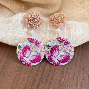 Macro detail of acrylic flower and butterfly pendant earrings with vintage floral relief