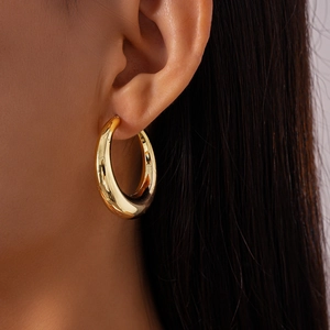 Close-up of a glossy gold C-shaped hoop earring worn on a model's left ear lobe
