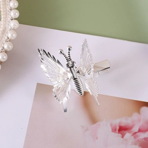 Close-up of silver metal butterfly hair clip with hollow wings and pearl necklace detail