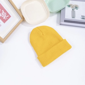 Flat lay of a bright yellow knitted beanie with a minimalist wooden frame and ceramic decor