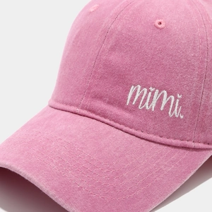 Close-up of pink washed cotton baseball cap featuring mimi embroidery and stitched brim