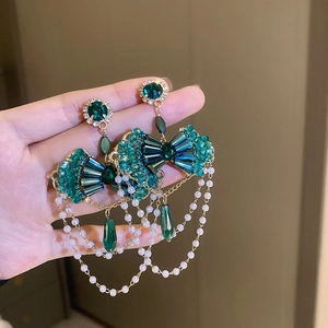 Vintage gold earrings with green crystals and white pearl fringe tassels in a hand shot