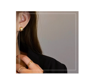 Detail of chunky gold hoop earrings and layered rings on model with polished finish