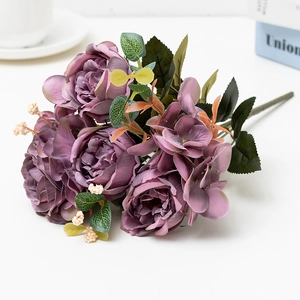 Close-up of purple artificial rose bouquet with silk petals and green leaves on white desk