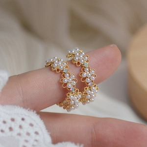 Detail view of dainty gold wire flower earrings with white pearls on a model's finger