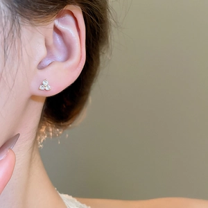 Close-up of small zircon flower stud earrings worn on ear with golden base finish