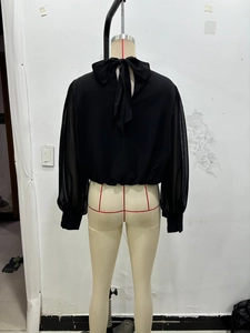 Détail du haut en mousseline noire avec manches en organza et grand nœud décoratif au col
