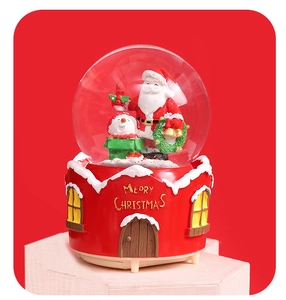 Close-up of a Christmas snow globe with Santa and snowman on a red house base