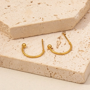 Detailed view of gold-plated C-shaped earrings with minimalist beads on stone surface