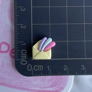 Detailed view of a mini yellow resin envelope charm on a measuring mat for DIY crafts
