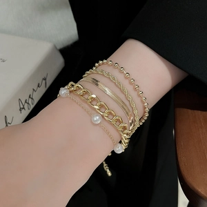 Close-up of golden multi-layer bracelets with pearls and various link textures on wrist