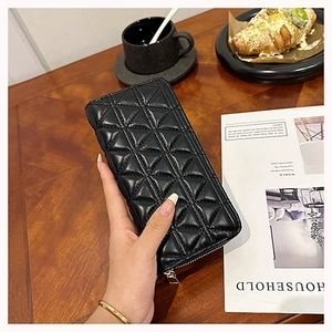 Quilted long black leather wallet held over a desktop with a coffee and bread scene