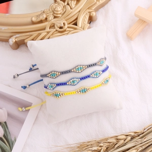 Three bohemian woven seed bead bracelets in grey, blue and yellow on white pillow