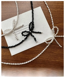 Detailed view of three bow necklaces with black, white, and baroque pearls on wood surface
