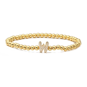 Detailed macro of gold beaded stretch bracelet with cubic zirconia letter W charm