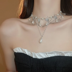 Detail of layered silver necklace with bow design and teardrop pearl on model neck