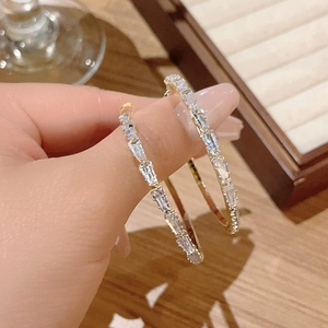 Close-up of gold hoop earrings with baguette-cut zircon stones held in hand