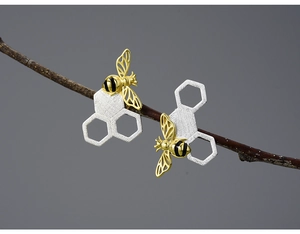 Macro shot of 925 silver honeycomb earrings with golden bee on natural branch